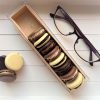 chocolate macrons in an open case next to a set of looking glasses